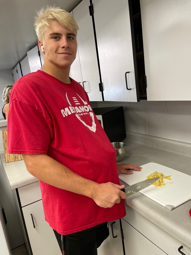 Dalton Shuda wearing the pregnancy simulator for Parenting class and practicing knife skills for spinach artichoke bites